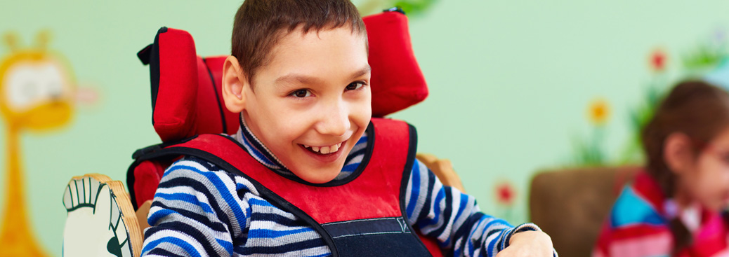 Background image of a boy with a physical disability sitting in a harness chair smiling