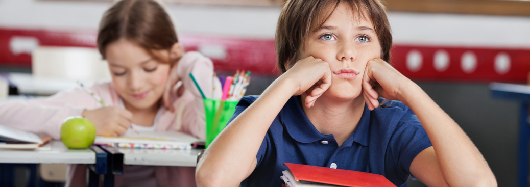 lms-primary-bg-83 Male primary school student sitting at desk looking fowards into the distance, resting cheeks on hands