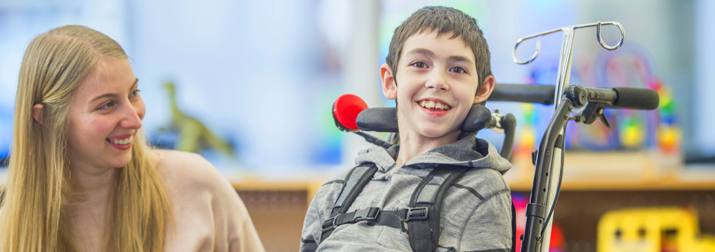 secondary-banner-1 Banner image of a female teacher smiling at a boy with a physical disability sitting in a specialised wheelchair